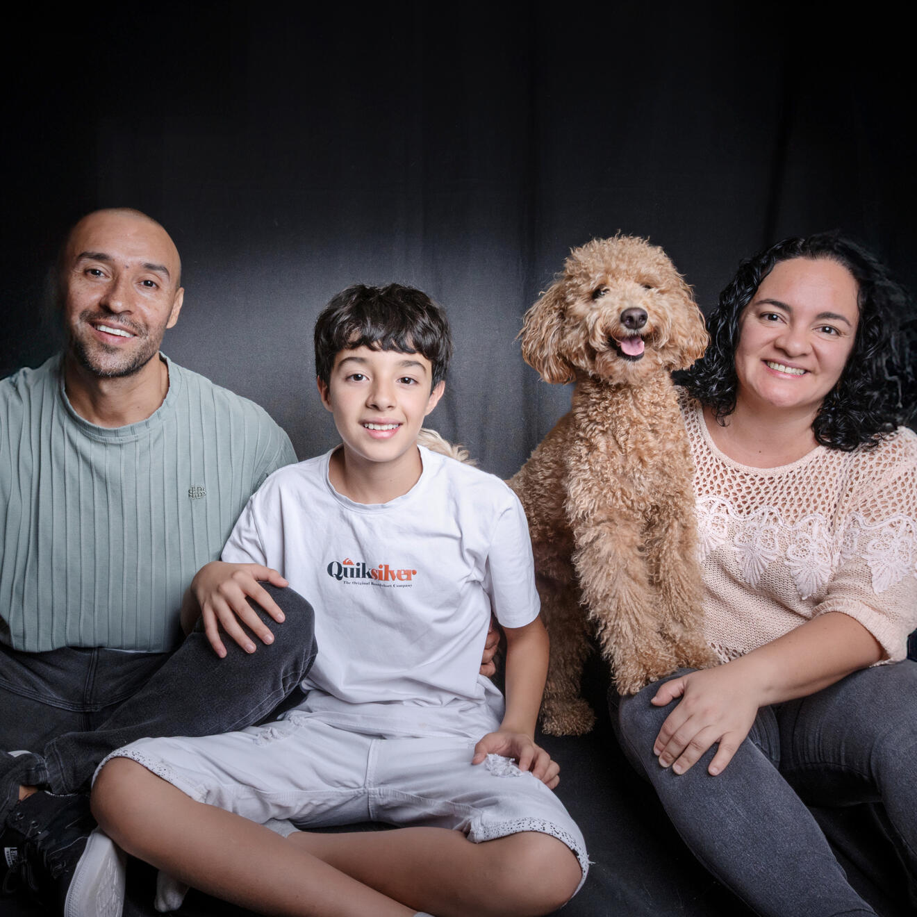 Family with their dog smiling together outdoors on a sunny day.