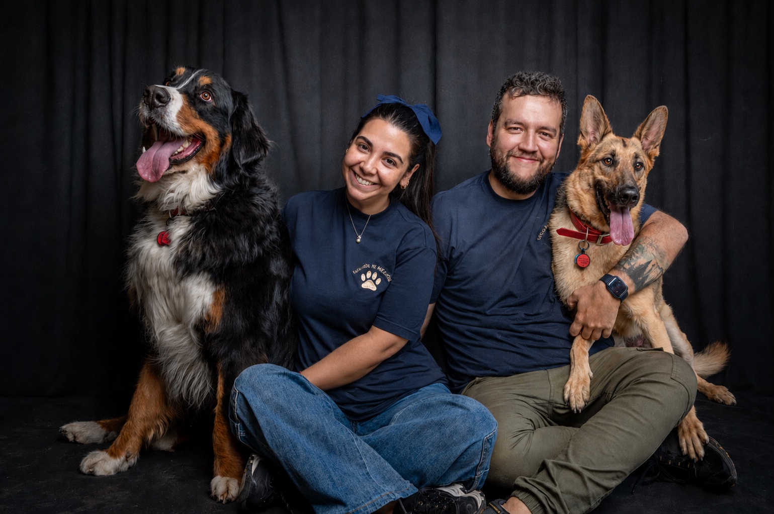 Ana and Andrés seated in their studio with a Bernese mountain dog and a German shepherd